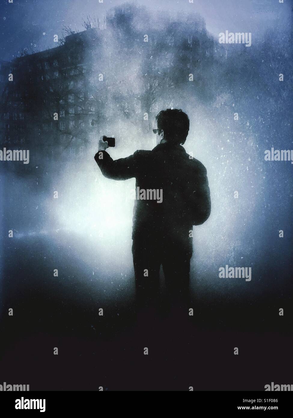 Blau getönten schwarz-weiß Foto mit dramatische Beleuchtung ein Mann hält seine Kamera-Handy auf Armlänge beim posieren für ein Selbstporträt. Stockfoto