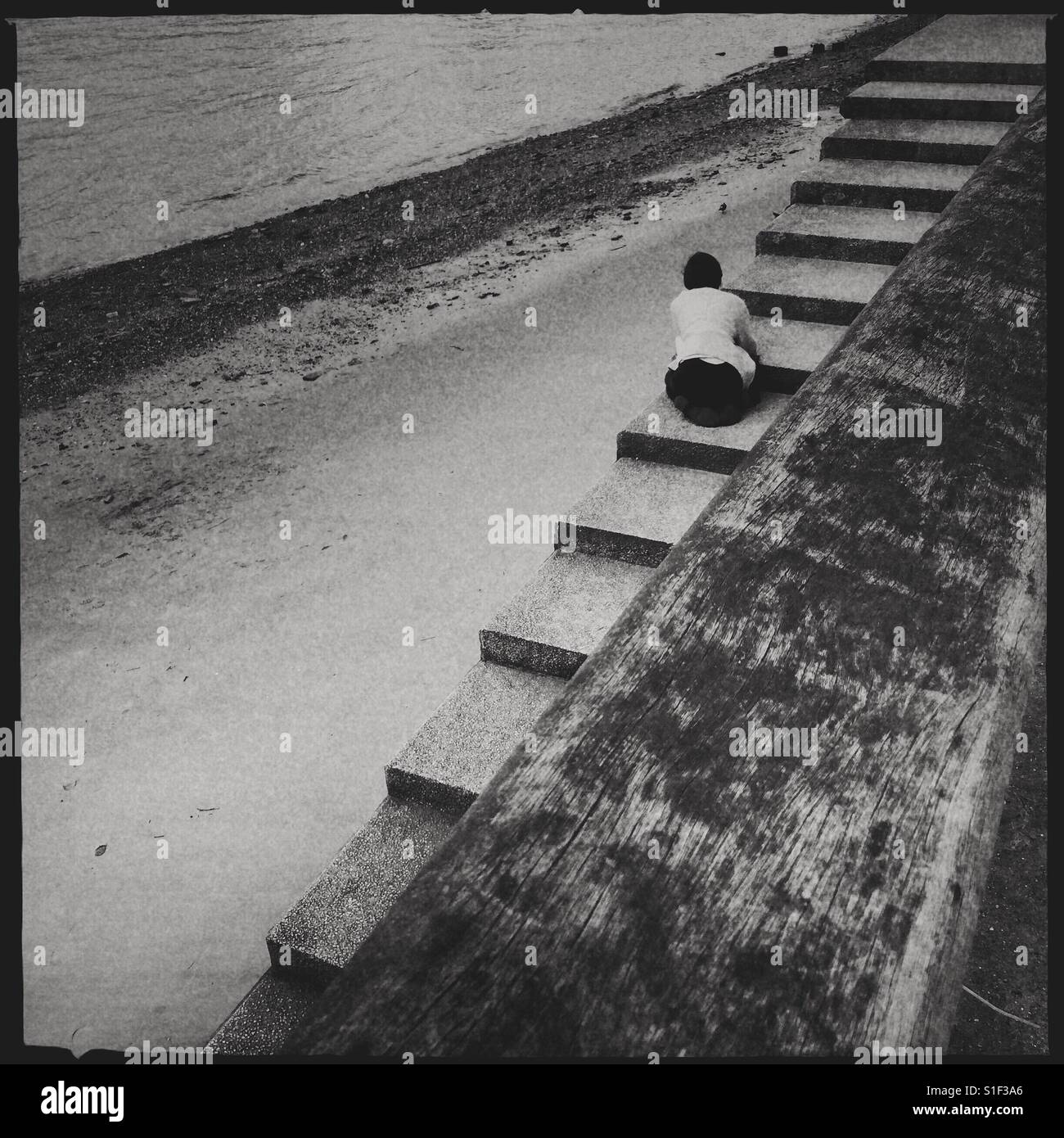 Schwarz-weiß Foto eines einsamen Frau sitzt auf einige Schritte, die mit dem Rücken zum Betrachter blickt in ein Gewässer. Stockfoto