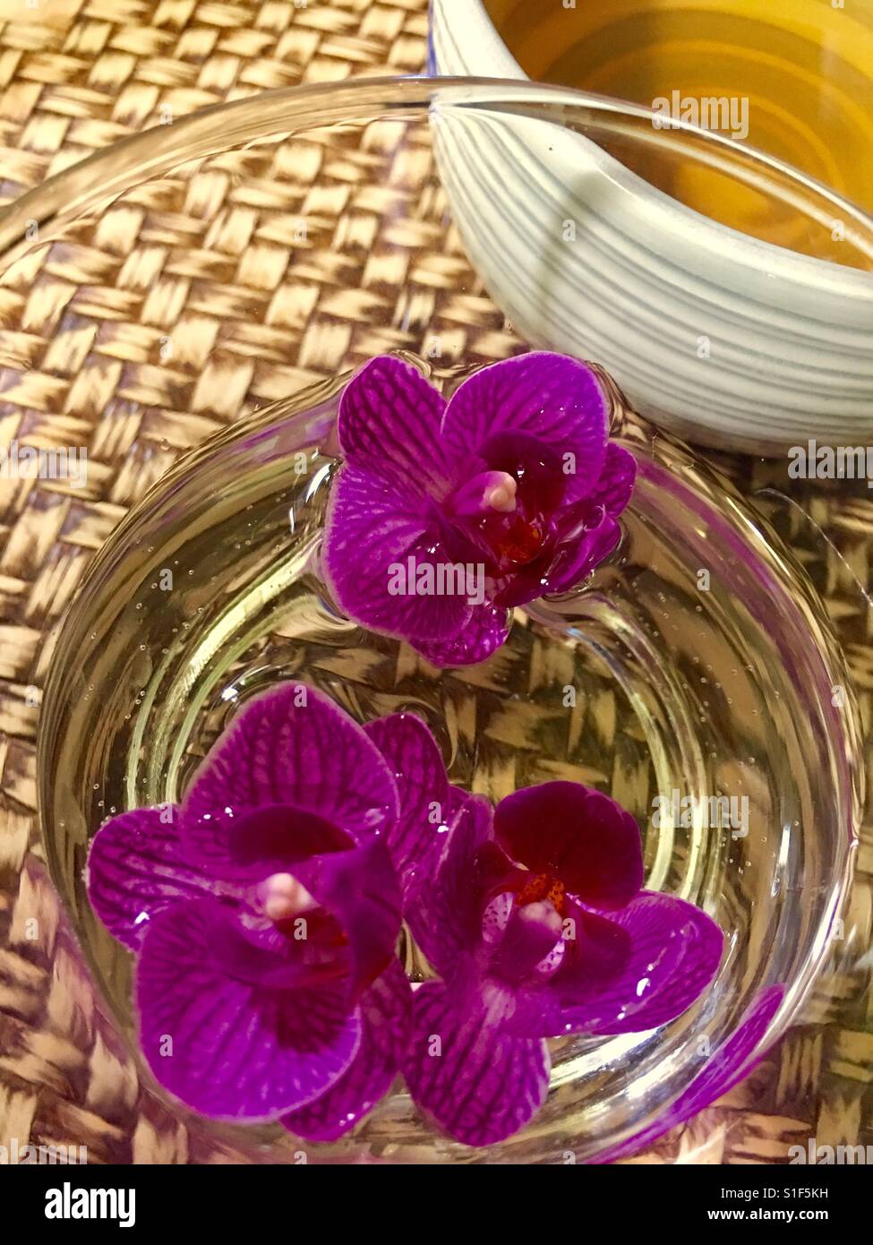 Lila rosa Orchideen mit eine Tasse grüner Tee gegen vietnamesische gewebte Tablett - Smartphone-aufgenommenes Stockfoto