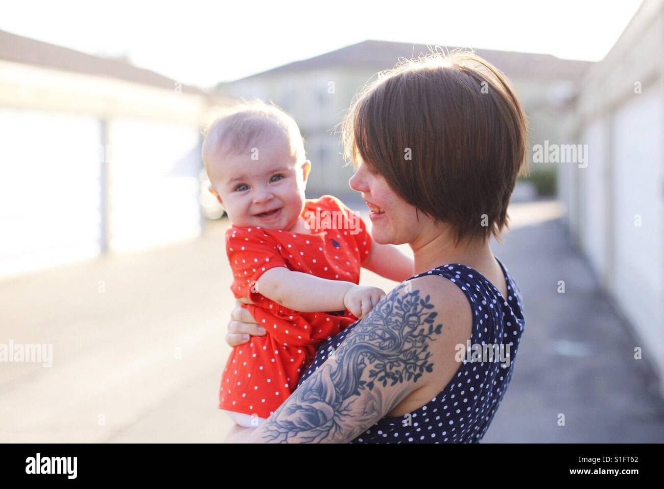 Hippe junge Mutter mit Tattoos und kurze Haare Baby Tochter glücklich hielt Stockfoto