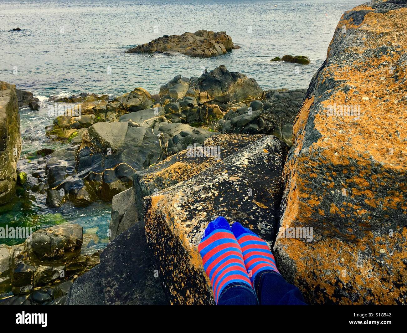 Füße in gestreiften Socken auf den Felsen am Strand Stockfoto