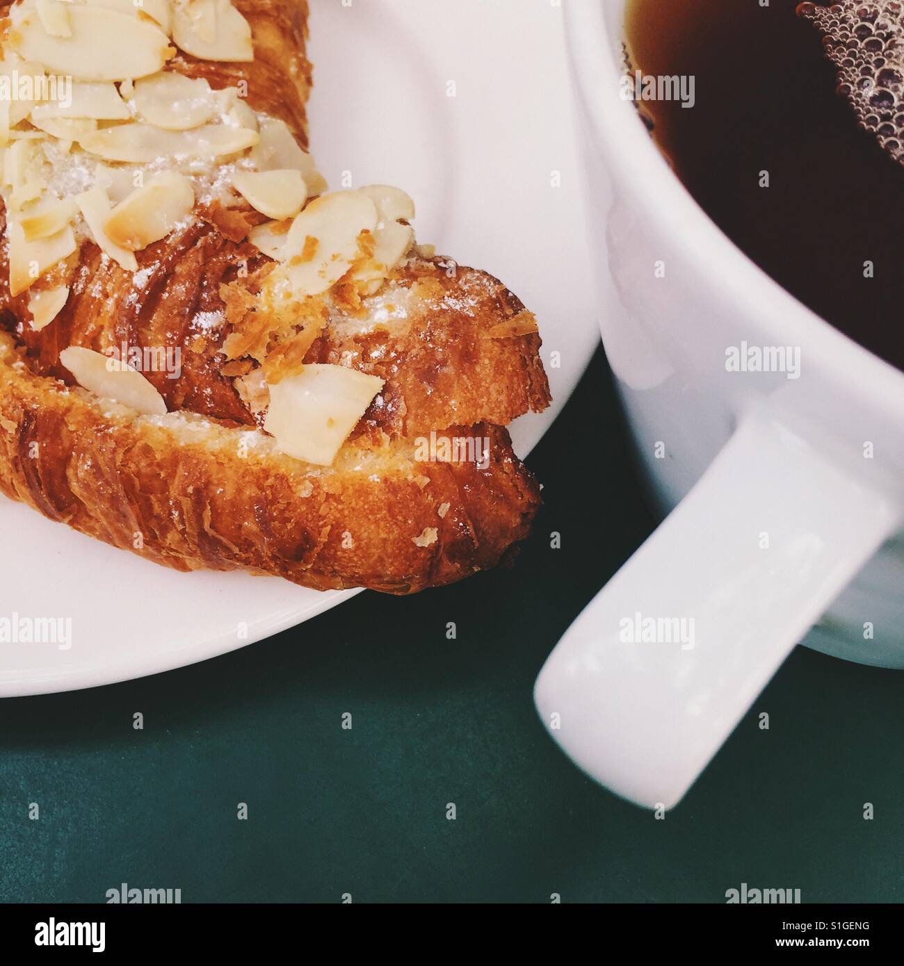 Eine frische Tasse Earl Grey Tee und eine Mandel Croissant am grünen Tisch Stockfoto
