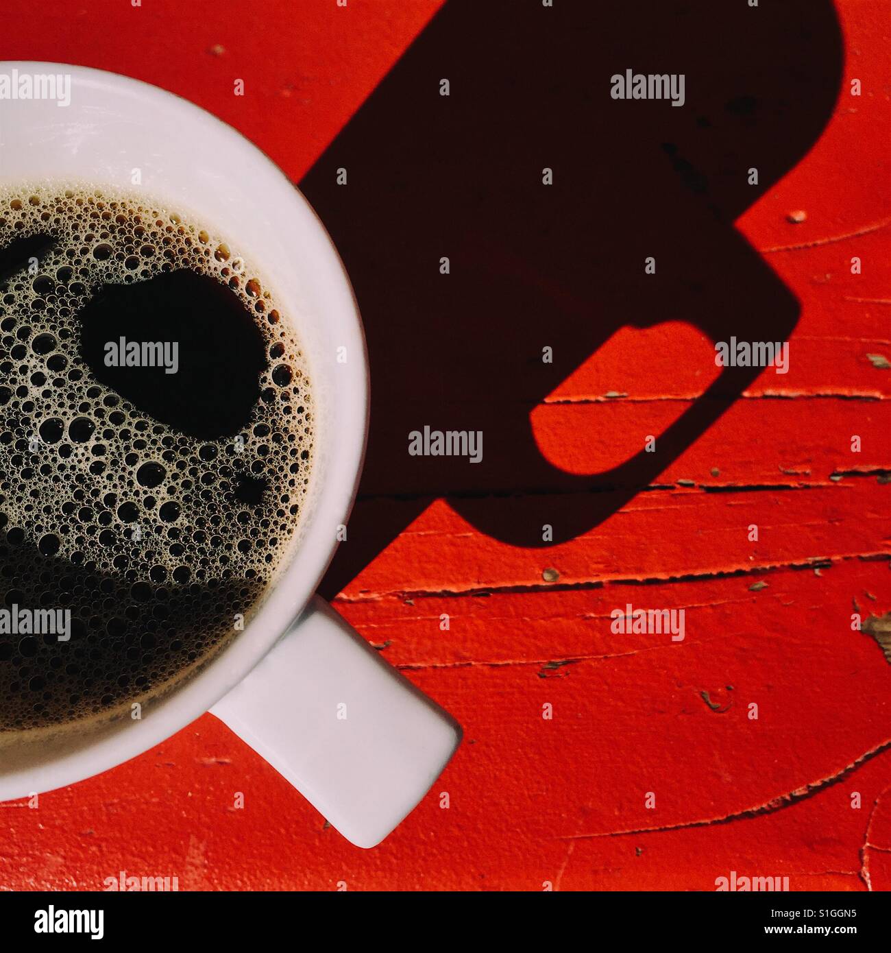 Eine obenliegende Nahaufnahme Schuss von einer frischen Tasse schwarzen Kaffee auf einem roten Holztisch. Eine einfache Komposition mit einem dunklen Schatten Stockfoto