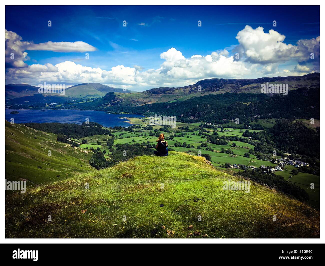 Eine Frau mit roten Haaren sitzt an der Spitze der Katze Glocken Hügel im Lake District, mit Blick auf Derwentwater. Stockfoto