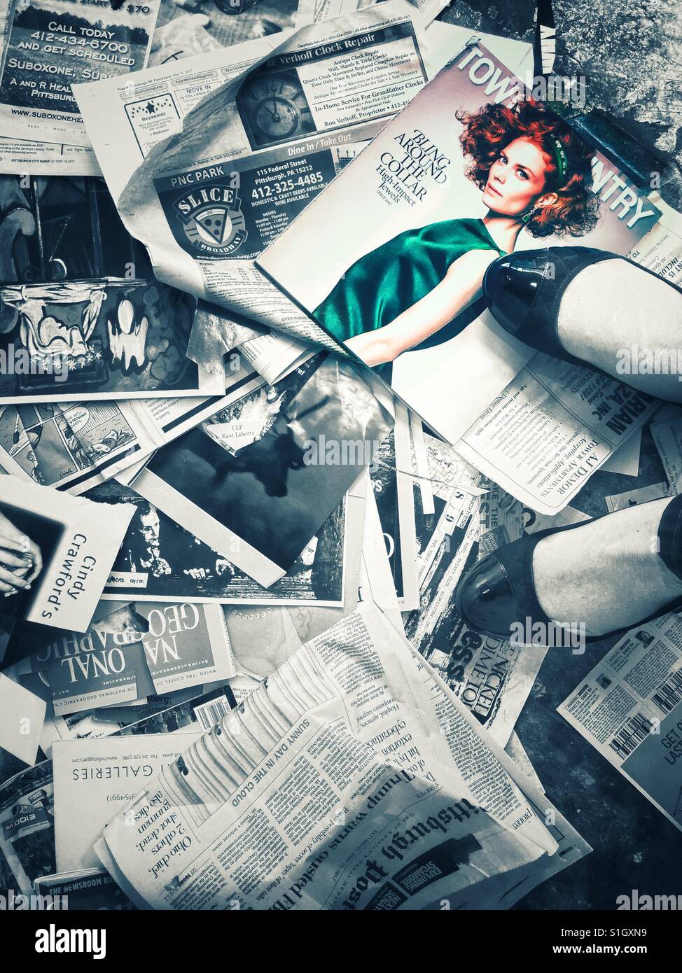 Eine Frau die Füße stehen auf einer großen Anzahl von Zeitschriftenseiten und Ausschnitte, die verstreut in den Boden, mit einem Bild von roten Haaren Fotomodell in Farbe Stockfoto