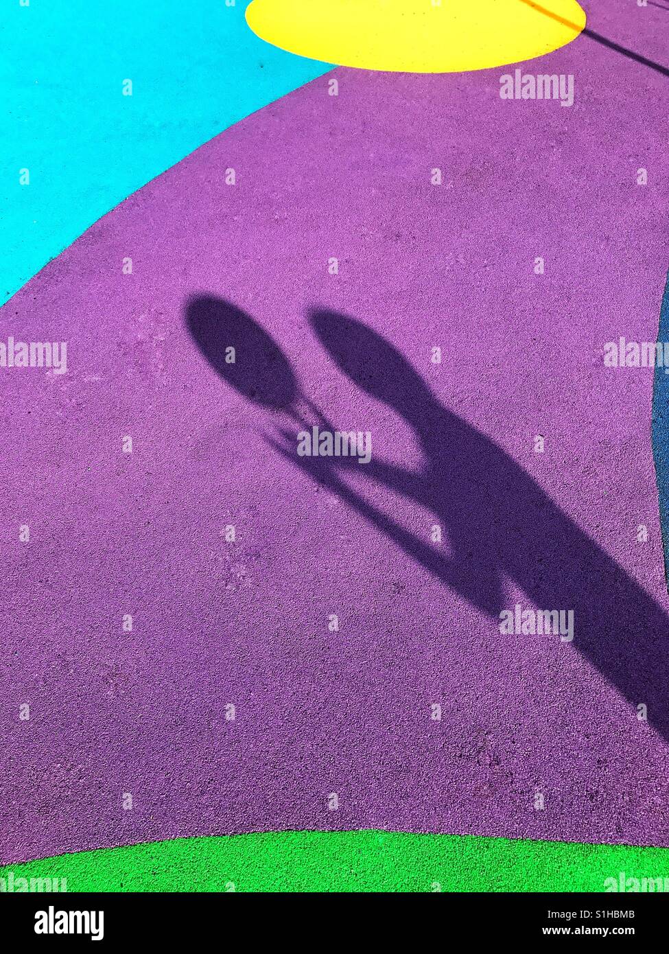 Der Schatten eines 7-jährigen Jungen ist im bunten Stock eines Spielplatzes. Der junge wirft einen Ball und steht kurz davor, ihn zu fangen. Ein Bild mit Mehrfachnutzen. Foto Credit © COLIN HOSKINS. - Smartphone-aufgenommenes Stockfoto