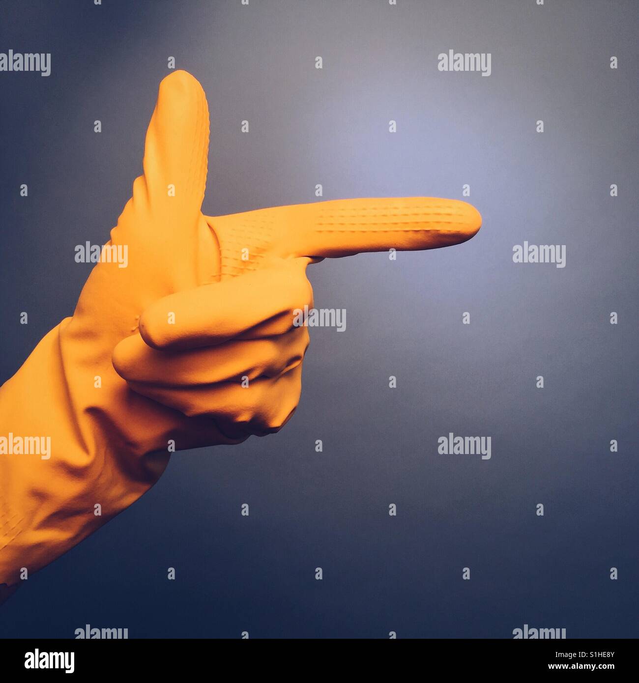 Die Hand eines Mannes in einem gelben Gummihandschuh macht eine Geste auf blauem Grund die hand zeigen Stockfoto