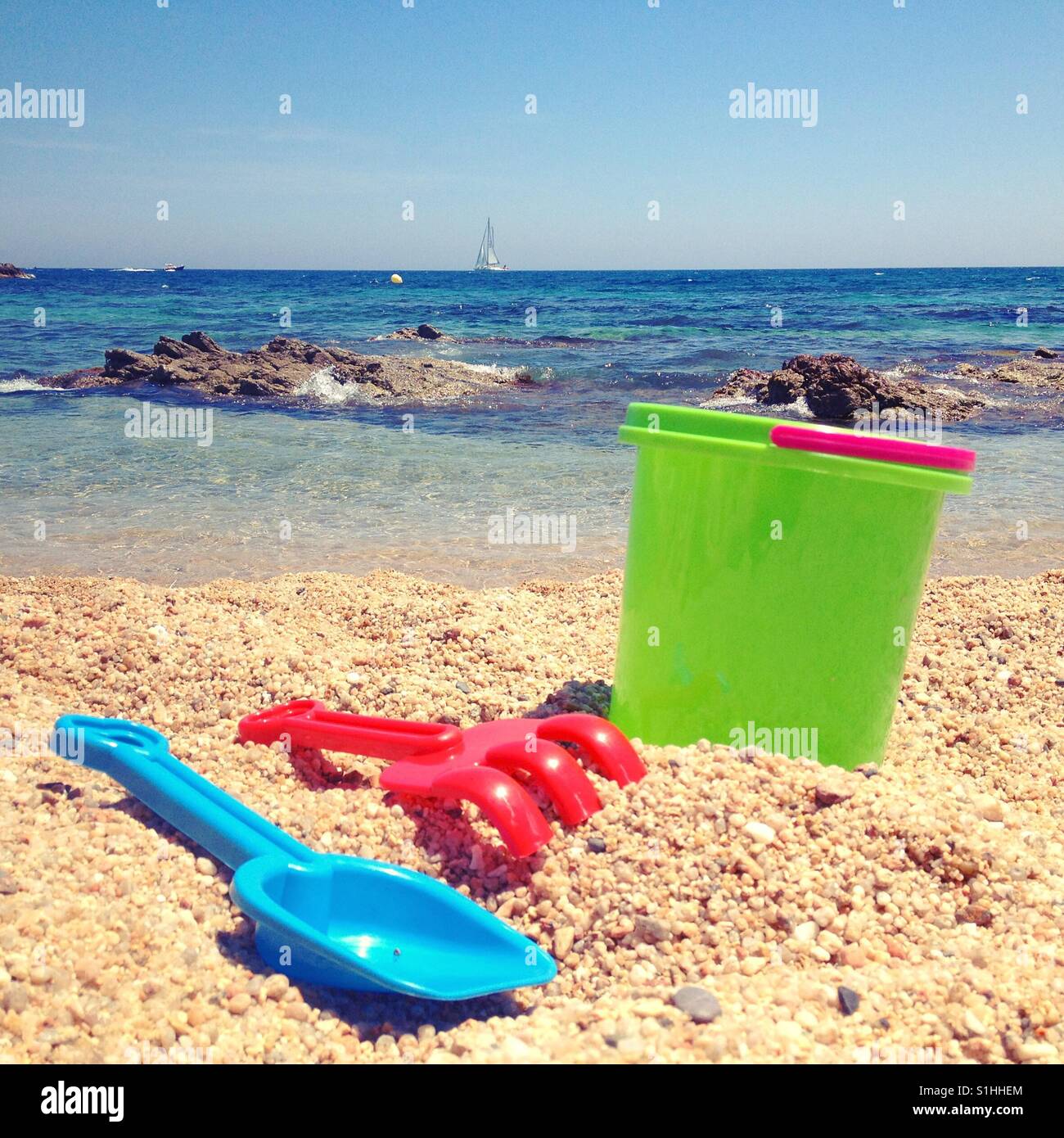 Sommer-Szene am Strand mit Spielzeug auf dem Sand und Segelboot im Meer. Stockfoto