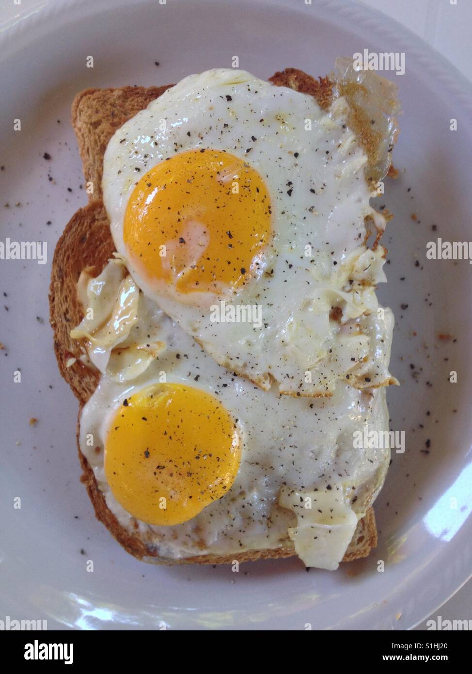 Nahaufnahme von zwei Spiegeleier auf Vollkorn Toast mit einer Prise schwarzer Pfeffer (Hochformat). Weißen Teller, weißen Hintergrund. Von Matthew Oakes genommen. Stockfoto