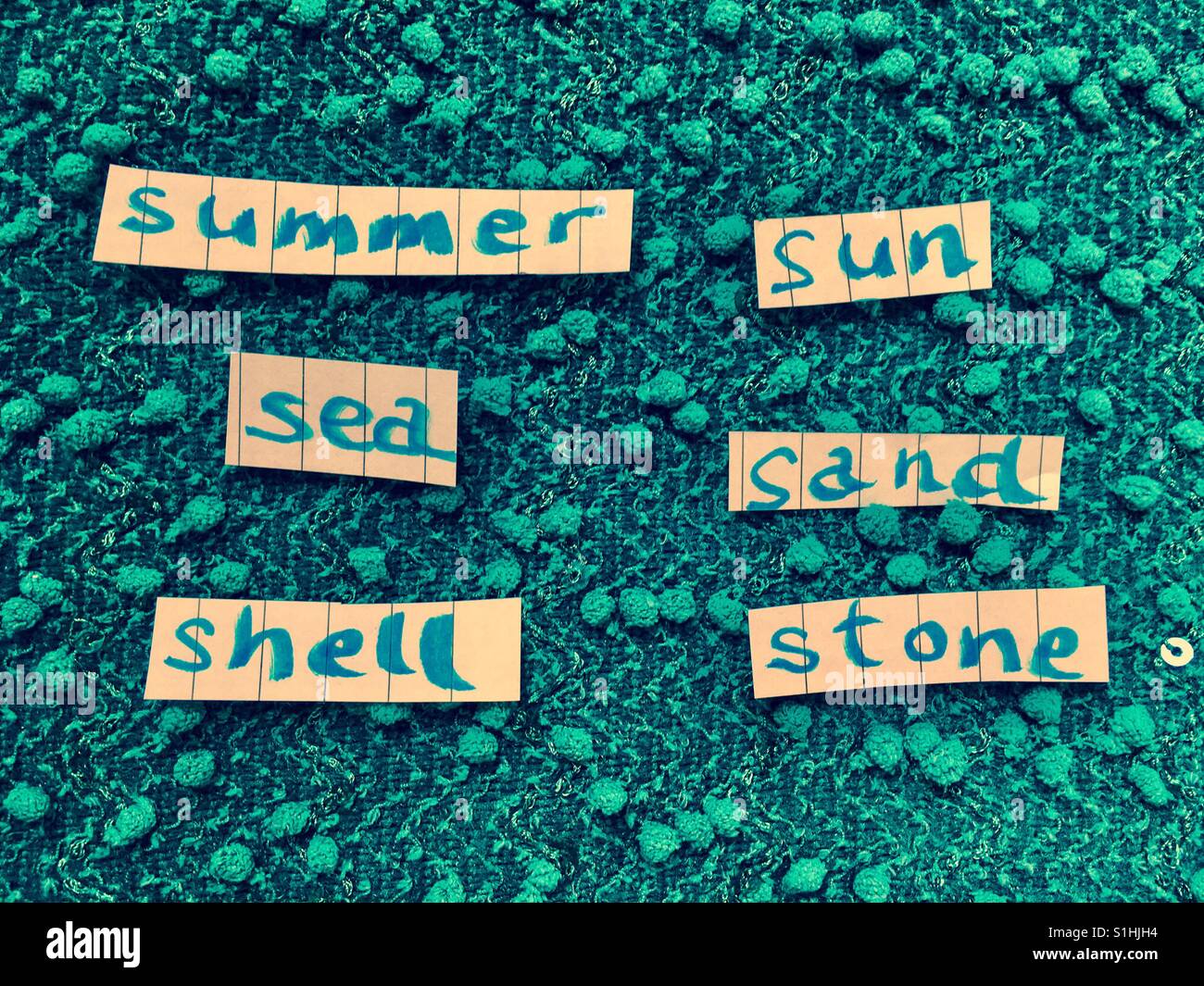 Sand Sea Shell Stein Sommersonne auf Stücke von Papier gegen strukturierten türkisfarbenen Hintergrund geschrieben - Smartphone-aufgenommenes Stockfoto