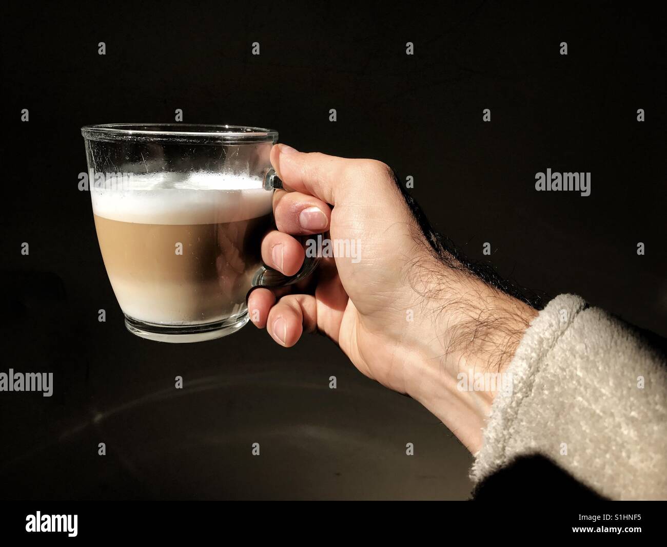 Mannes Hand mit einer Cappuccino-Tasse in der Morgensonne - Smartphone-aufgenommenes Stockfoto
