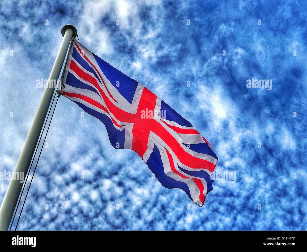 Der Union Jack Flagge fliegt hoch und stolz an einem windigen Tag im Sommer im Vereinigten Königreich. Das rote Kreuz des Heiligen Georg ist deutlich sichtbar. Bildnachweis - © COLIN HOSKINS. - Smartphone-aufgenommenes Stockfoto