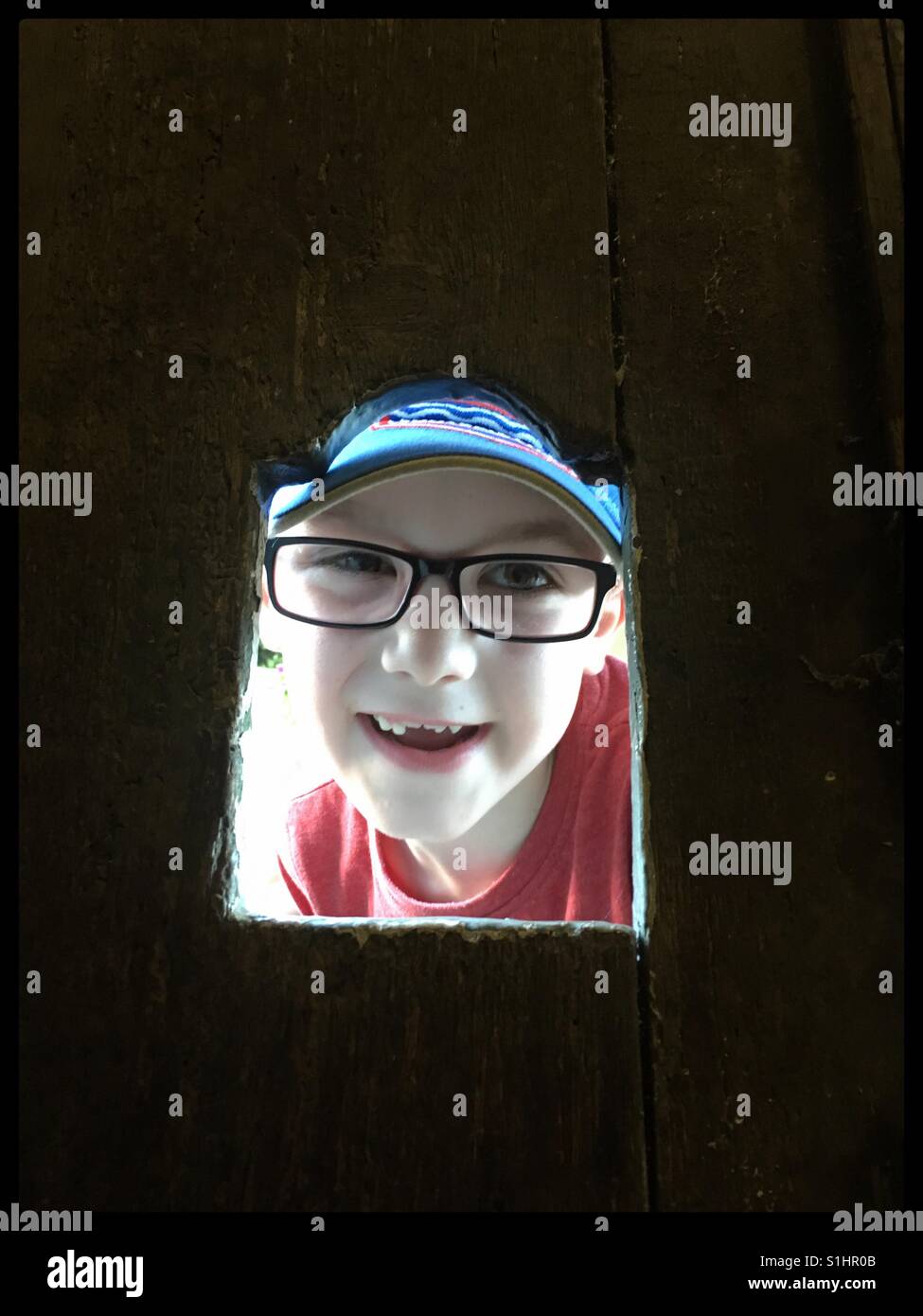 Junge Blick durch ein Loch in eine Holztür. Stockfoto