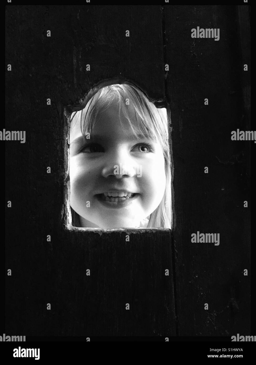 Mädchen Gesicht durch ein Loch in eine Holztür. Stockfoto