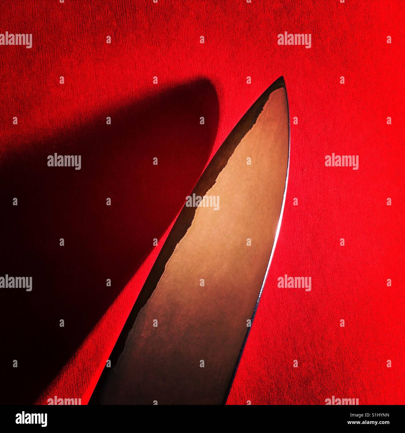 Die Klinge eines Messers auf eine rote Fläche mit einem tiefen Schatten Stockfoto