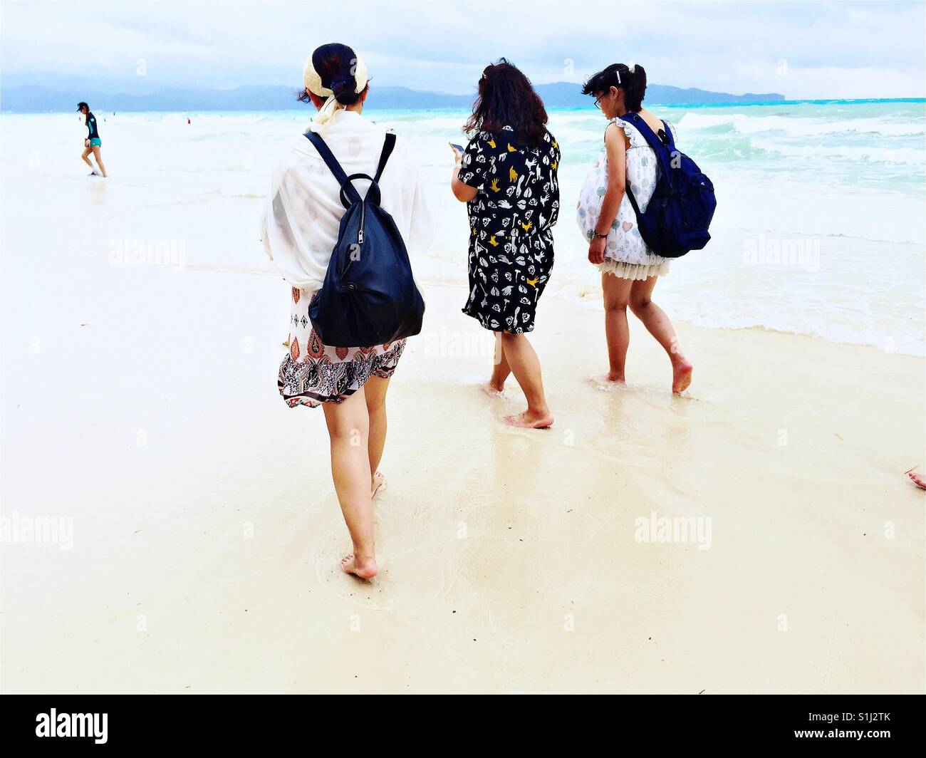 Drei barfüßige Frauen mit Rucksäcken zu Fuß auf der berühmten White Beach auf Boracay Island, Philippinen, während der Monsunzeit Stockfoto