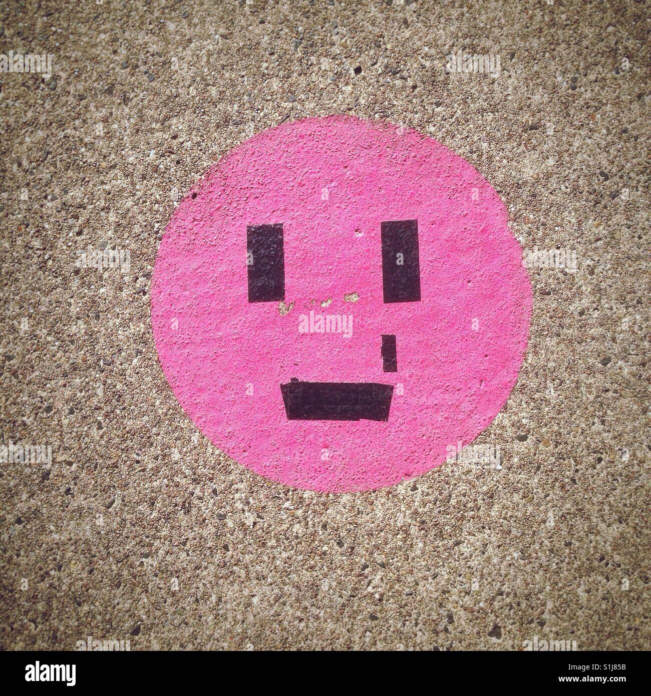 Ein trauriger Smiley Emoji erstellt mit Klebeband auf einem rosa Kreis auf dem Bürgersteig Stockfoto