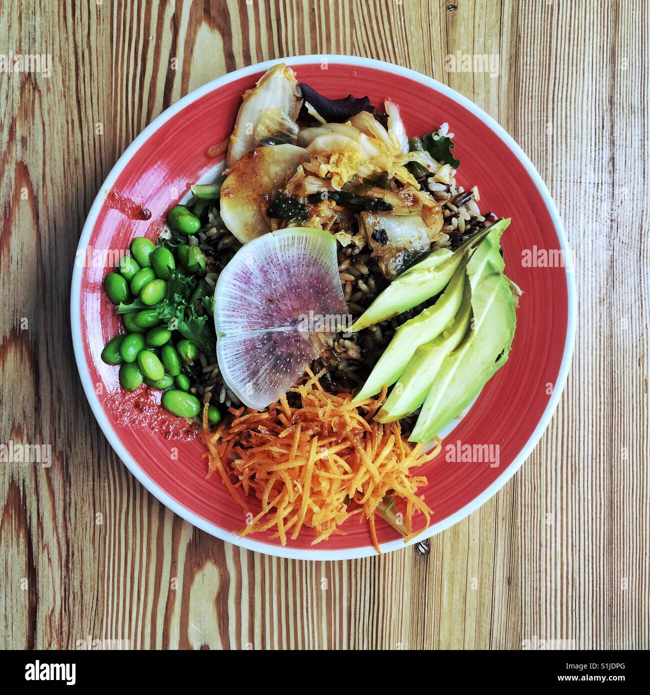 Gesunde vegane Reisschüssel mit Kimchi und Gemüse auf runde rote Platte sitzen auf Holztisch Draufsicht Stockfoto