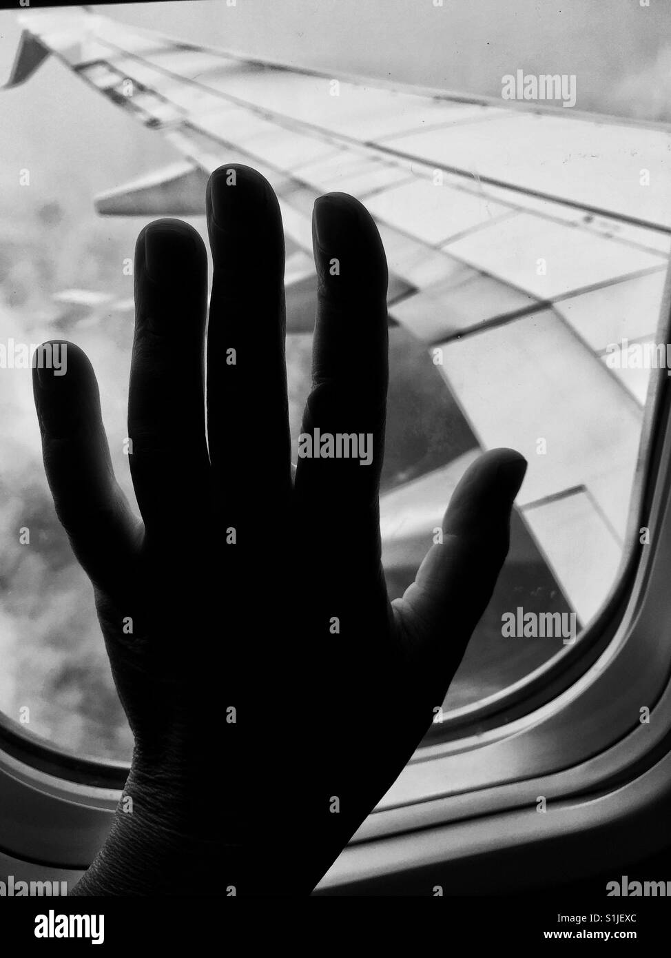 Hand berührt Flugzeugfenster mit Blick auf die Flügel Stockfoto