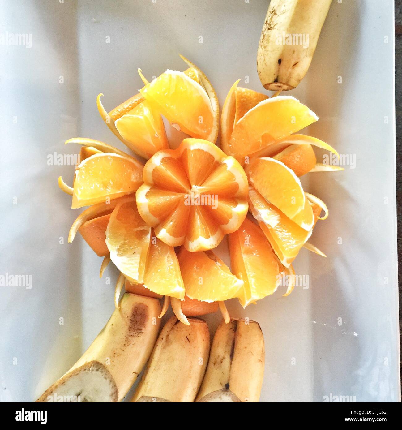 Orange künstlerisch geschnitten und präsentiert auf weißen Teller mit Bananen Stockfoto