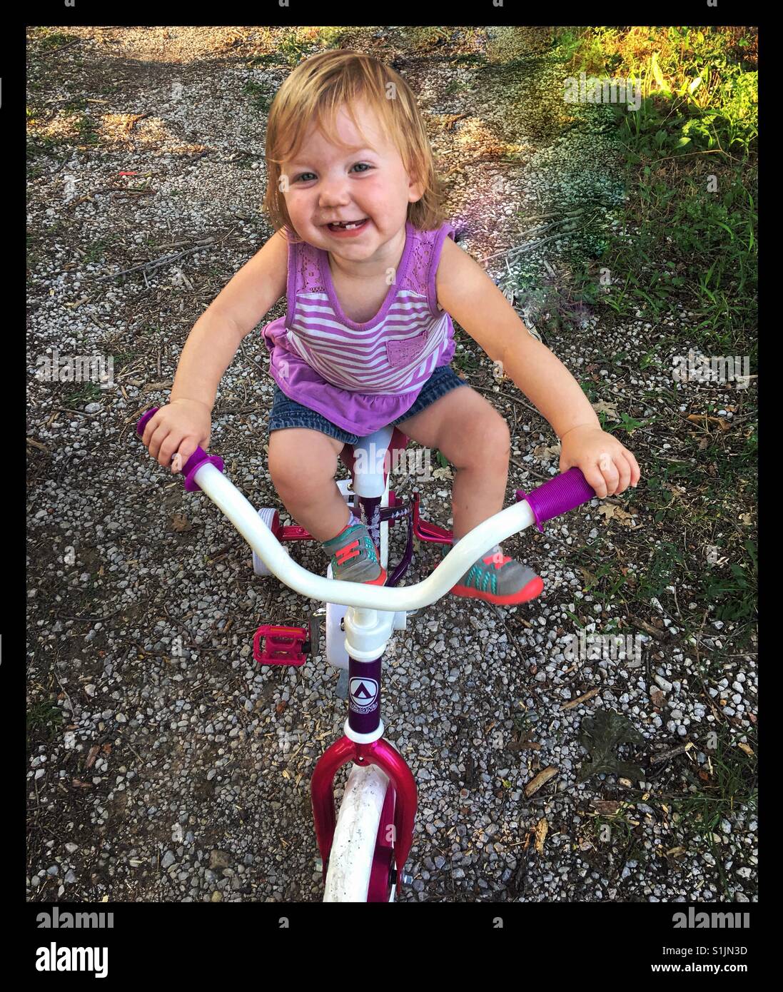 Glückliches kleine Mädchen klettert auf ihre Schwestern-Fahrrad, das viel zu groß für sie ist. Stockfoto