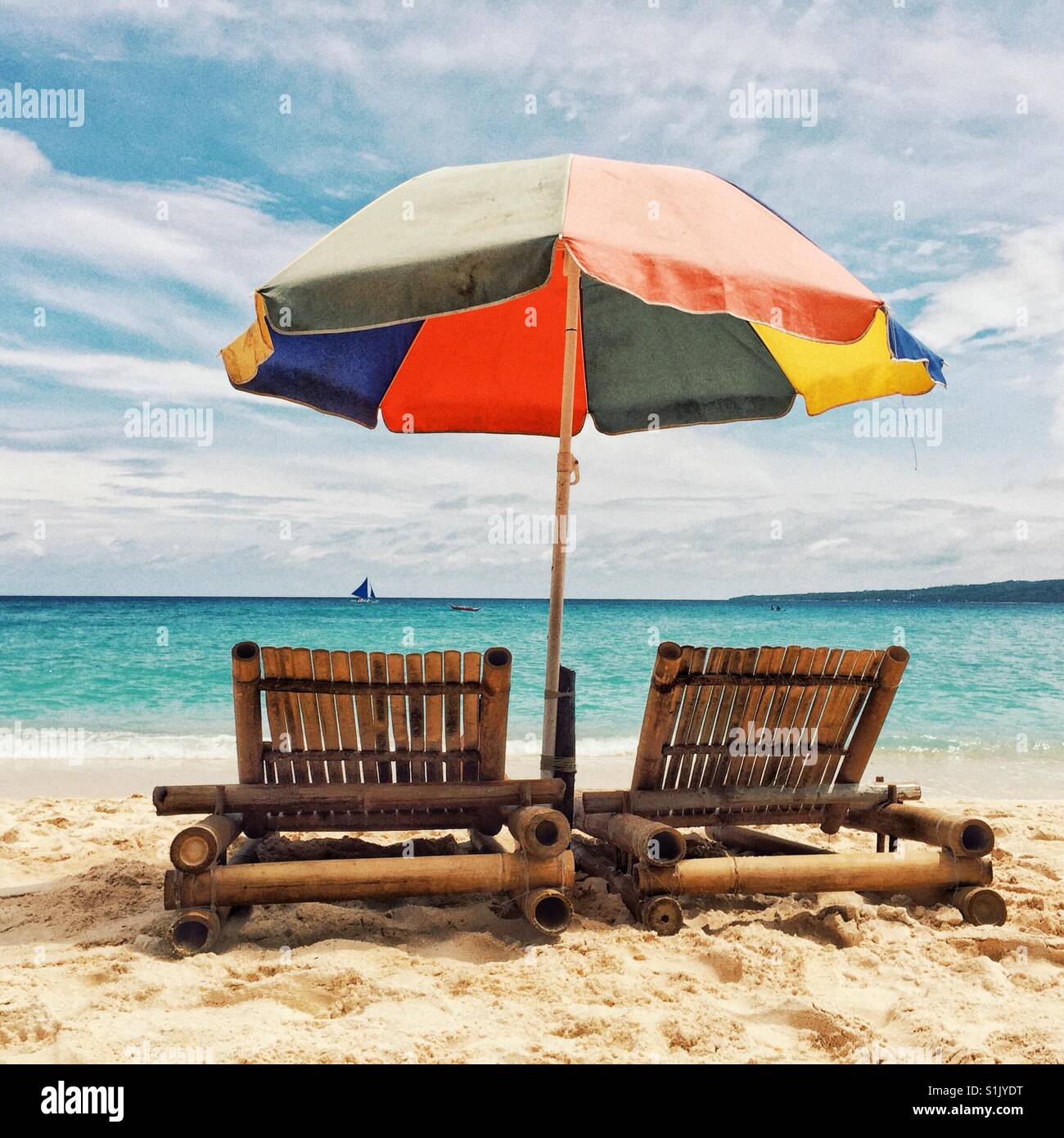 Zwei Bambus-Lounge-Stühle unter bunten Regenschirm auf einem Sand von Puka Beach auf der Insel Boracay, Philippinen Stockfoto
