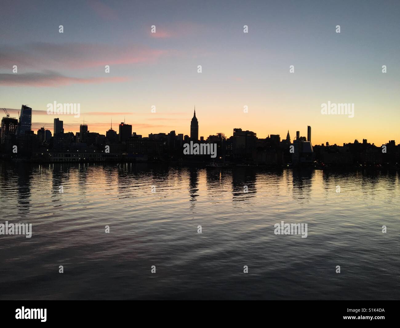 Skyline von Midtown Manhattan Silhouette gegen die Glut der Morgenröte Himmel zeigt ein bekanntes Wahrzeichen mit Reflexionen in das Stille Wasser des Hudson Rivers - Smartphone-aufgenommenes Stockfoto