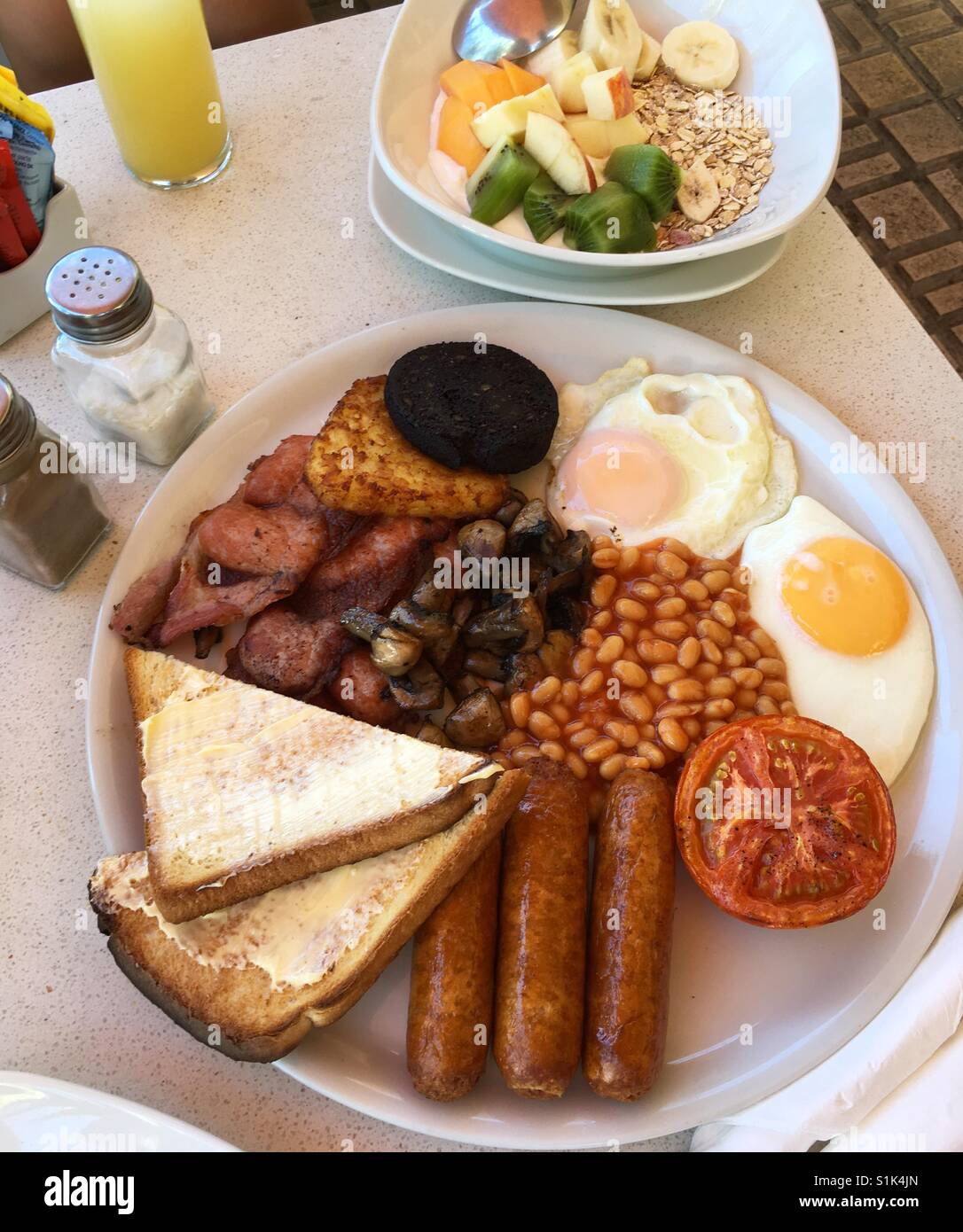 Englisches Frühstück mit Spiegeleiern, Bohnen, Toast und Müsli mit Obst Stockfoto