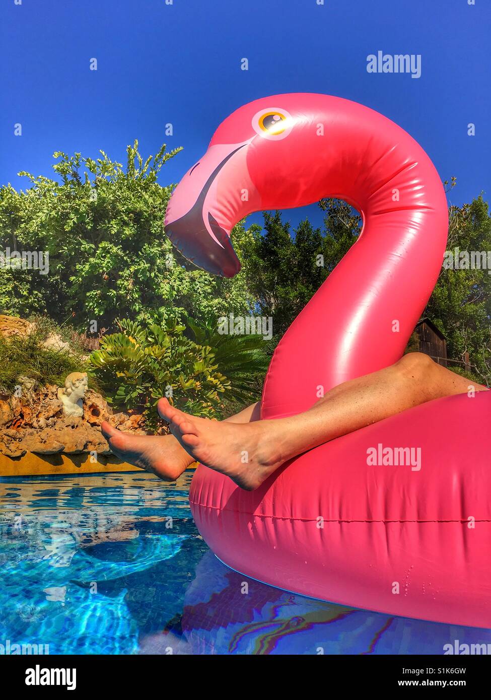 Sommer-Spaß. Füße und rosa aufblasbare Flamingo im Schwimmbad - Smartphone-aufgenommenes Stockfoto