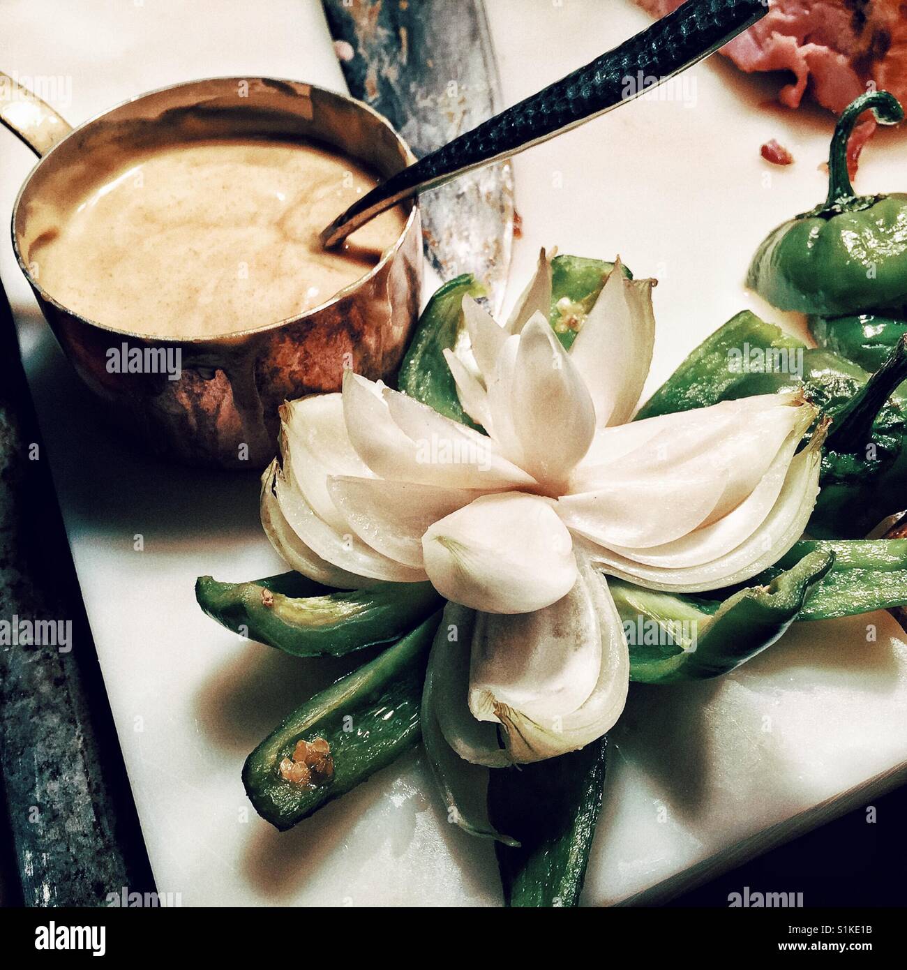 Weiße Zwiebel schneiden als Blume und präsentiert auf einem grünem Pfeffer neben der Sauce im Kupferkessel Stockfoto