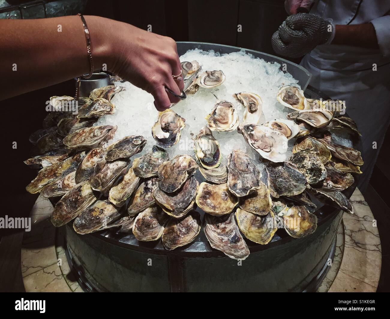 Frau Hand pflücken Auster aus dem großen Haufen davon auf Eis in einem restaurant - Smartphone-aufgenommenes Stockfoto