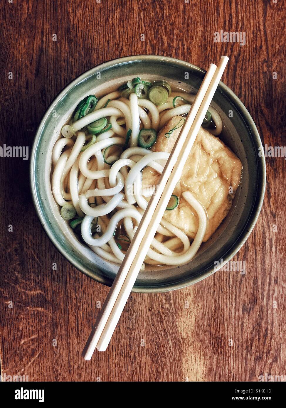 Klassische japanische Ramen-Suppe in Steinzeug Schale und Bambus Stäbchen oben auf rustikalen Holztisch - Smartphone-aufgenommenes Stockfoto