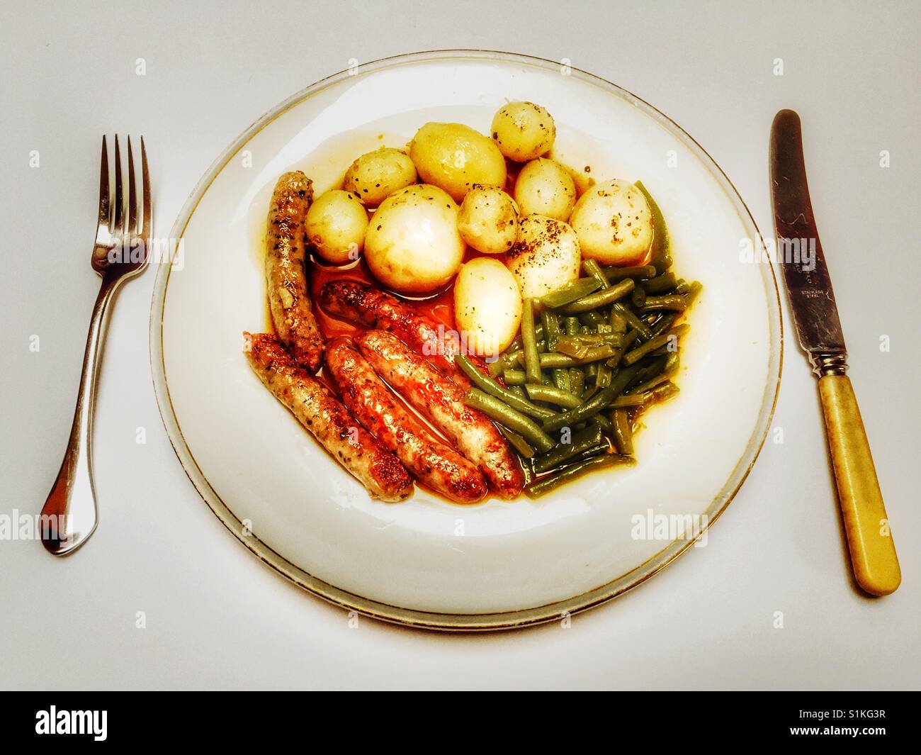 Chipolata-Würstchen, Frühkartoffeln, französische Stangenbohnen und Zwiebel Soße. - Smartphone-aufgenommenes Stockfoto