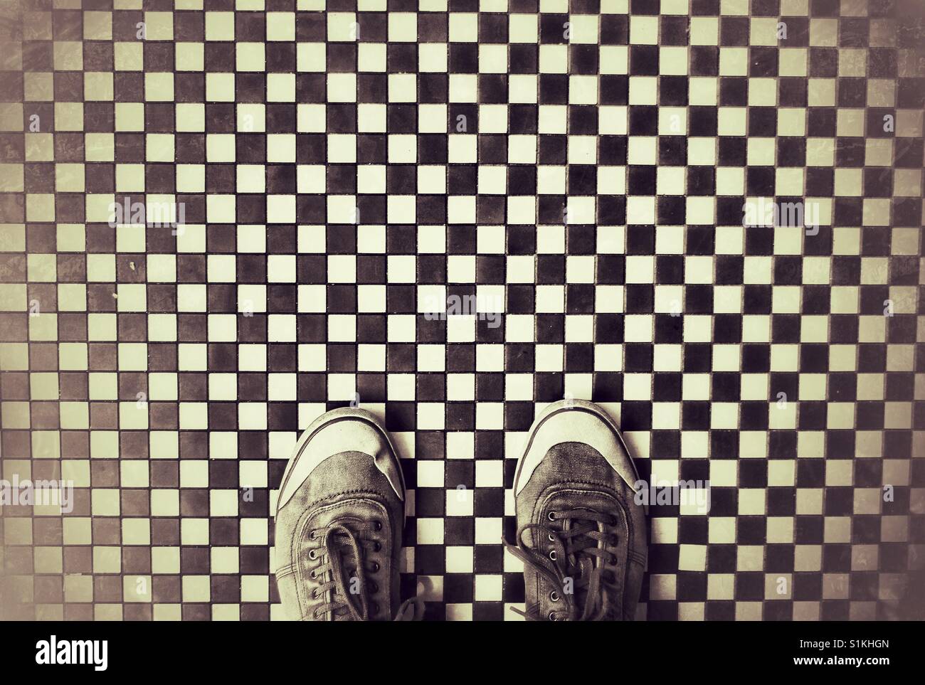 Blick von oben auf ein paar schwarze und weiße Schuhe stehen auf einem schwarz/weiß kariert und gefliest oder Mozaic Oberfläche Stockfoto