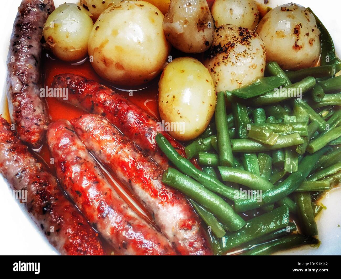 Chipolata-Würstchen, Kartoffeln, grüne Bohnen und Zwiebel Soße - Smartphone-aufgenommenes Stockfoto