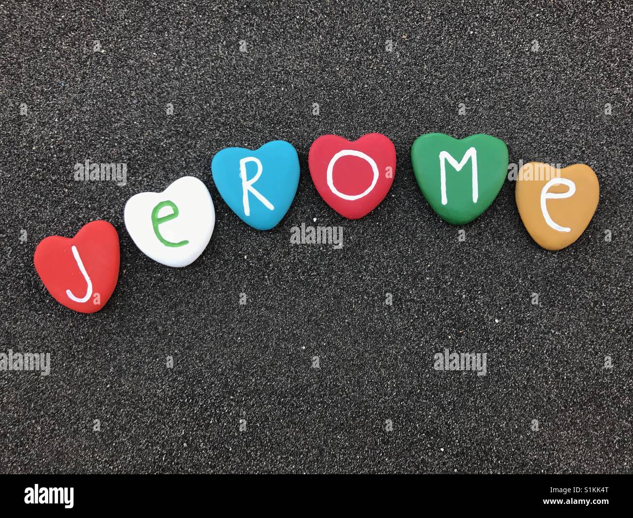 Jerome, französischer männlichen Vorname mit farbigen Herzen Steinen über schwarzen vulkanischen sand Stockfoto