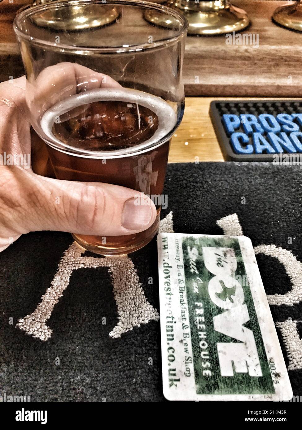 Die Hand eines Mannes hält einen halbes Pint Bier in einem englischen Pub. Stockfoto