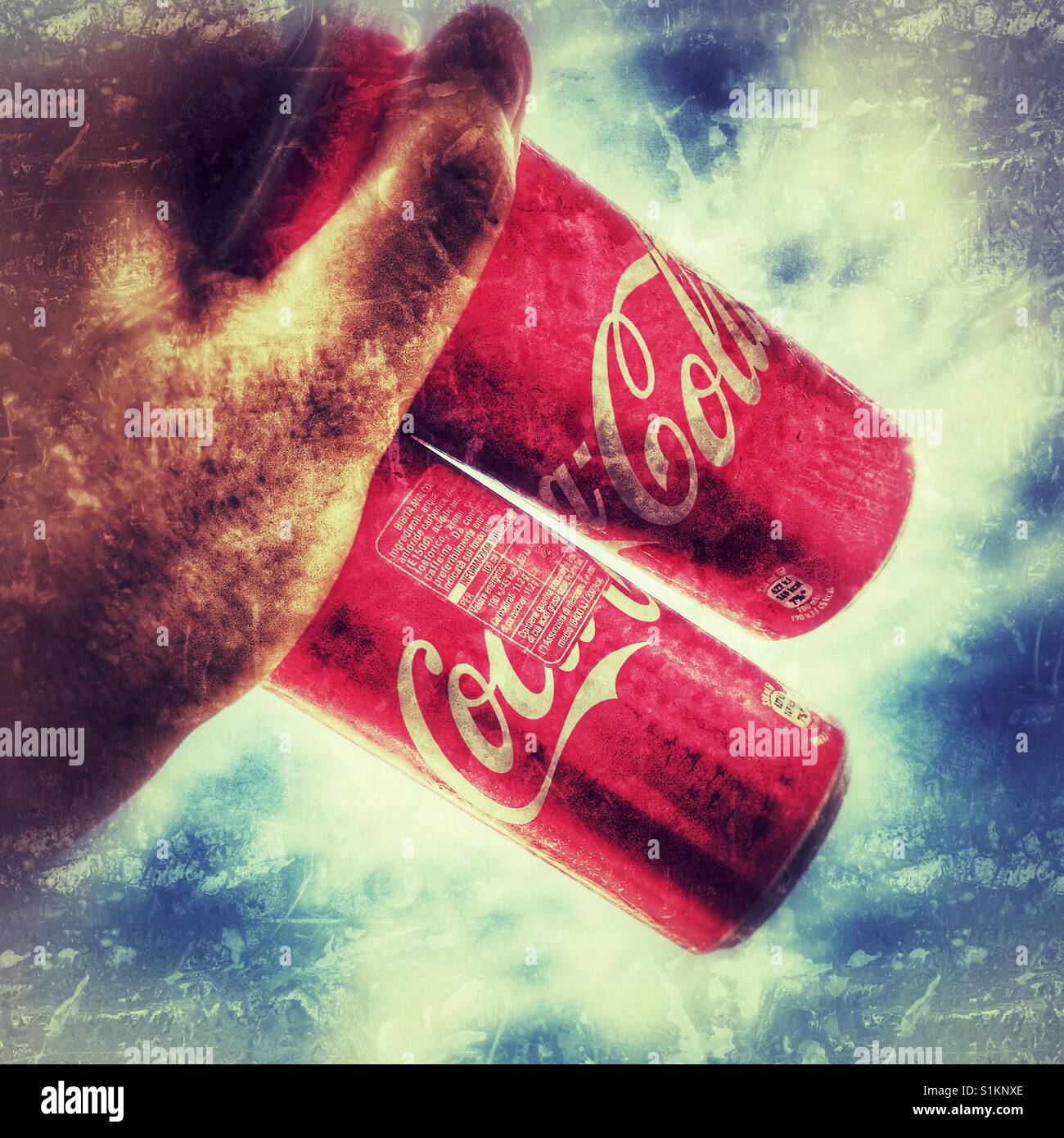 Coca Coladosen in der Hand über einen Himmelshintergrund - Smartphone-aufgenommenes Stockfoto