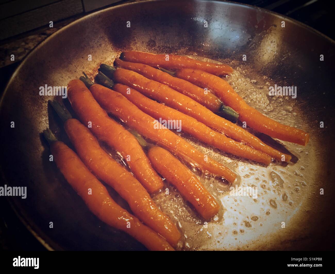 Erzeuger bis zum Verbraucher. Saisonale frisch geerntete Möhren in Butter simmering. Stockfoto
