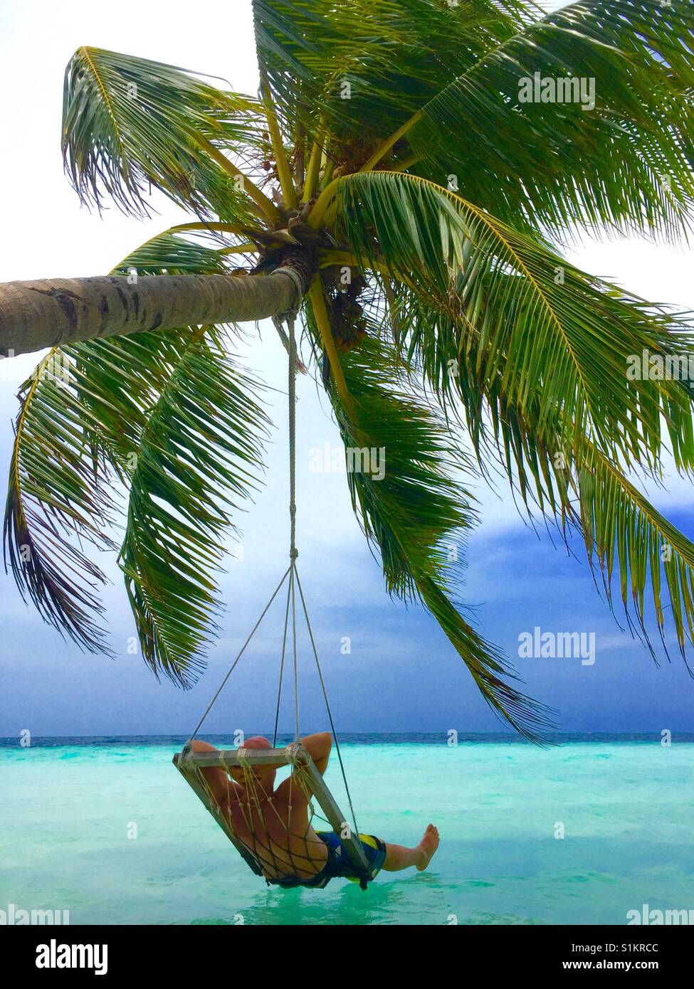 Junger Mann zum Entspannen in der Schaukel hängen von der Kokospalme über klares Wasser und genießen den Blick auf den Malediven. Stockfoto