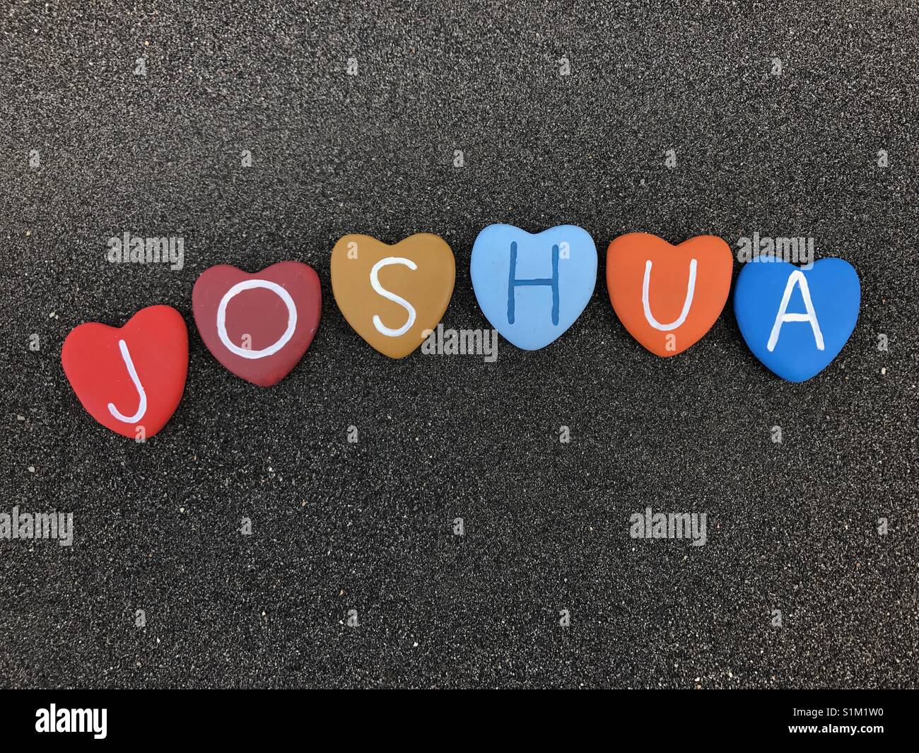 Joshua, männlich Name mit bunten Herzen Steine über schwarzen vulkanischen Sand Stockfoto