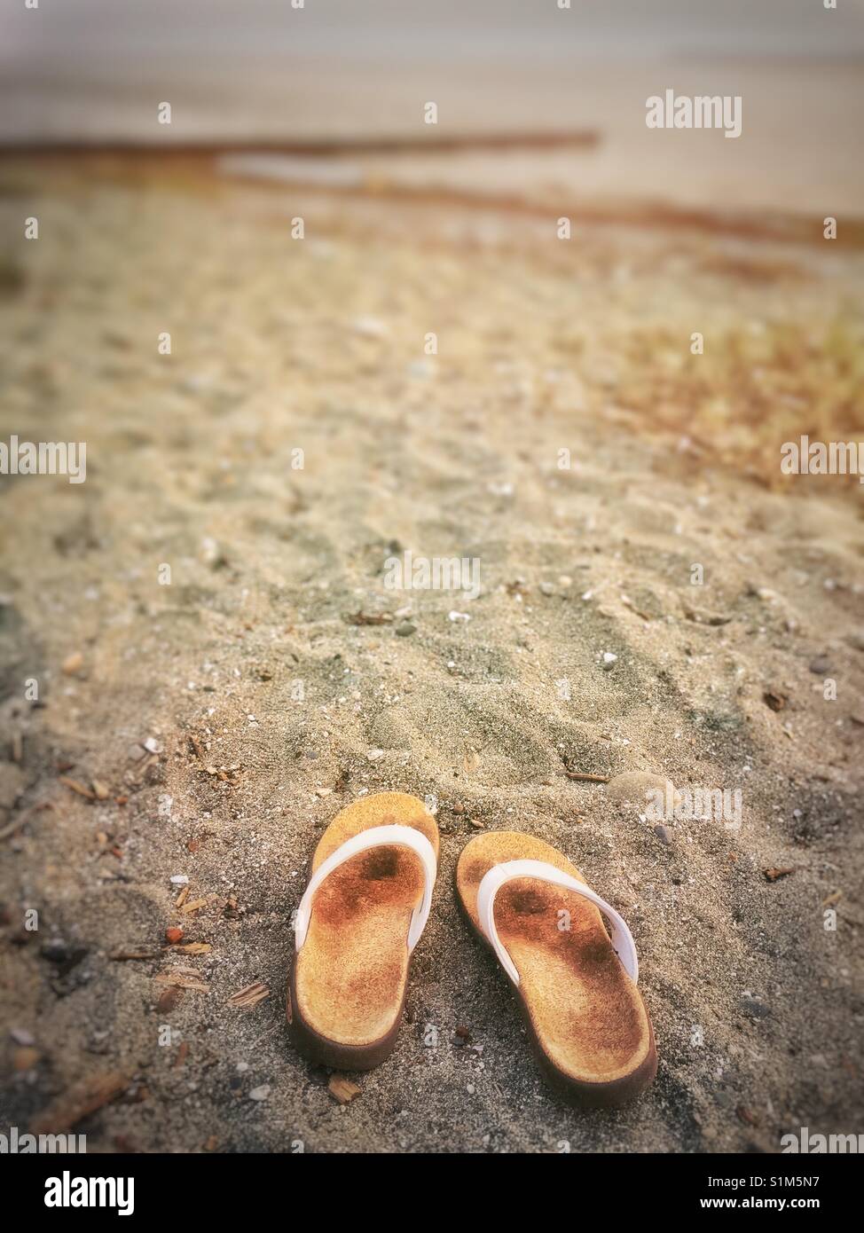 Weißen Stoff und Kork flip flop Sandalen sitzen auf einem Sandstrand. Crescent Beach, Surrey, British Columbia, Kanada. - Smartphone-aufgenommenes Stockfoto