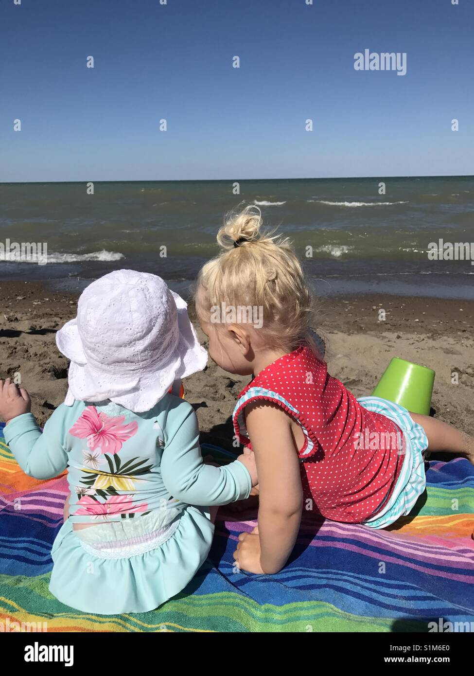 Zwei Kleine Mädchen In Badekleidung Sitzen Auf Einem Bunten Handtuch Am Strand Stockfotografie