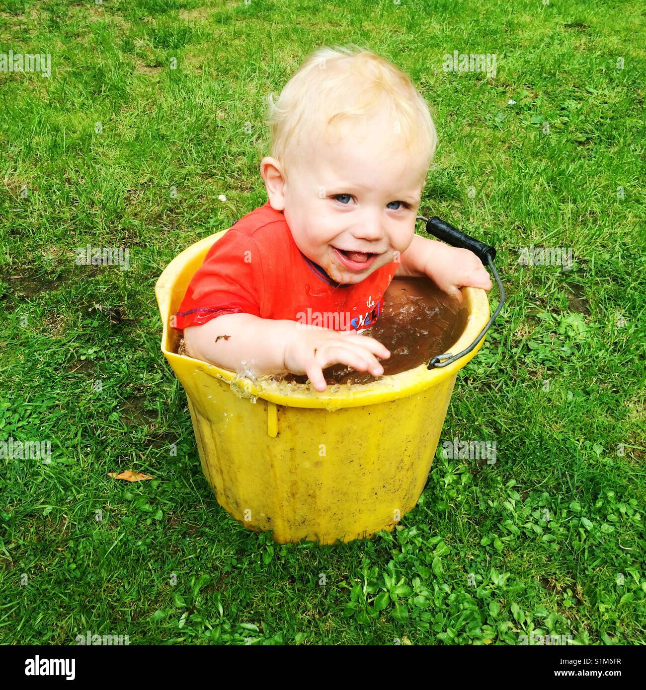 Elf Monate alten Baby boy in einen Eimer mit schmutzigem Wasser sitzen Stockfoto