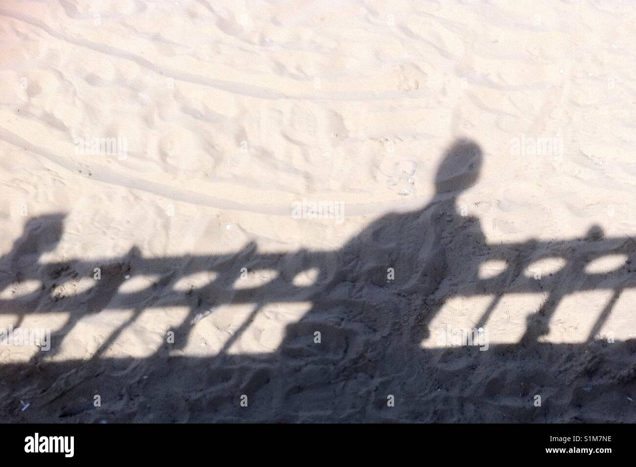 Schatten der Person über einen Zaun an einem Sandstrand. Stockfoto