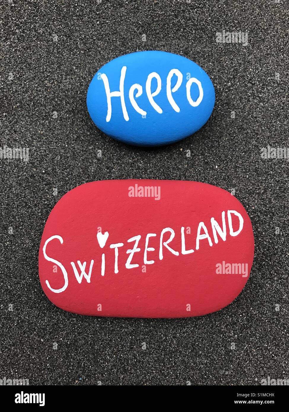 Hallo Schweiz mit geschnitzten und farbigen Steinen über schwarzen vulkanischen Sand Stockfoto