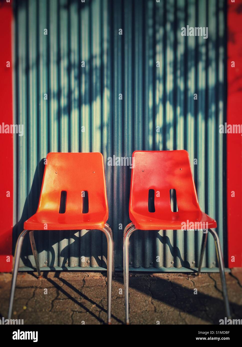 Zwei helle orange retro Plastikstühle gegen einen Farbverlauf blau Wellblech Wand. Stockfoto