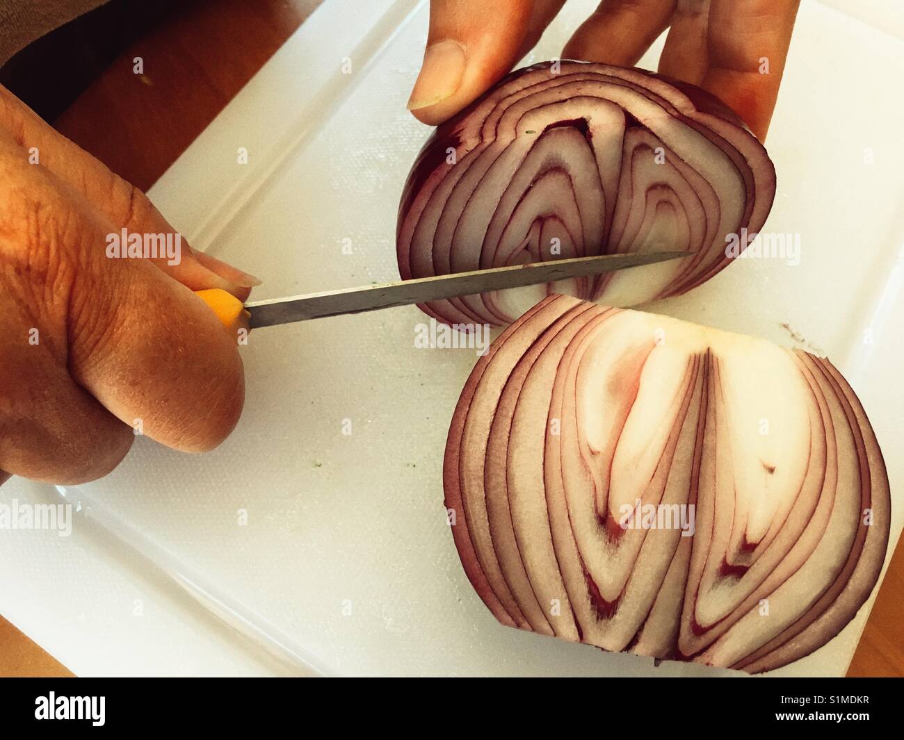 Das Schneiden einer Zwiebel in der Hälfte auf einem weißen Schneidebrett - Smartphone-aufgenommenes Stockfoto