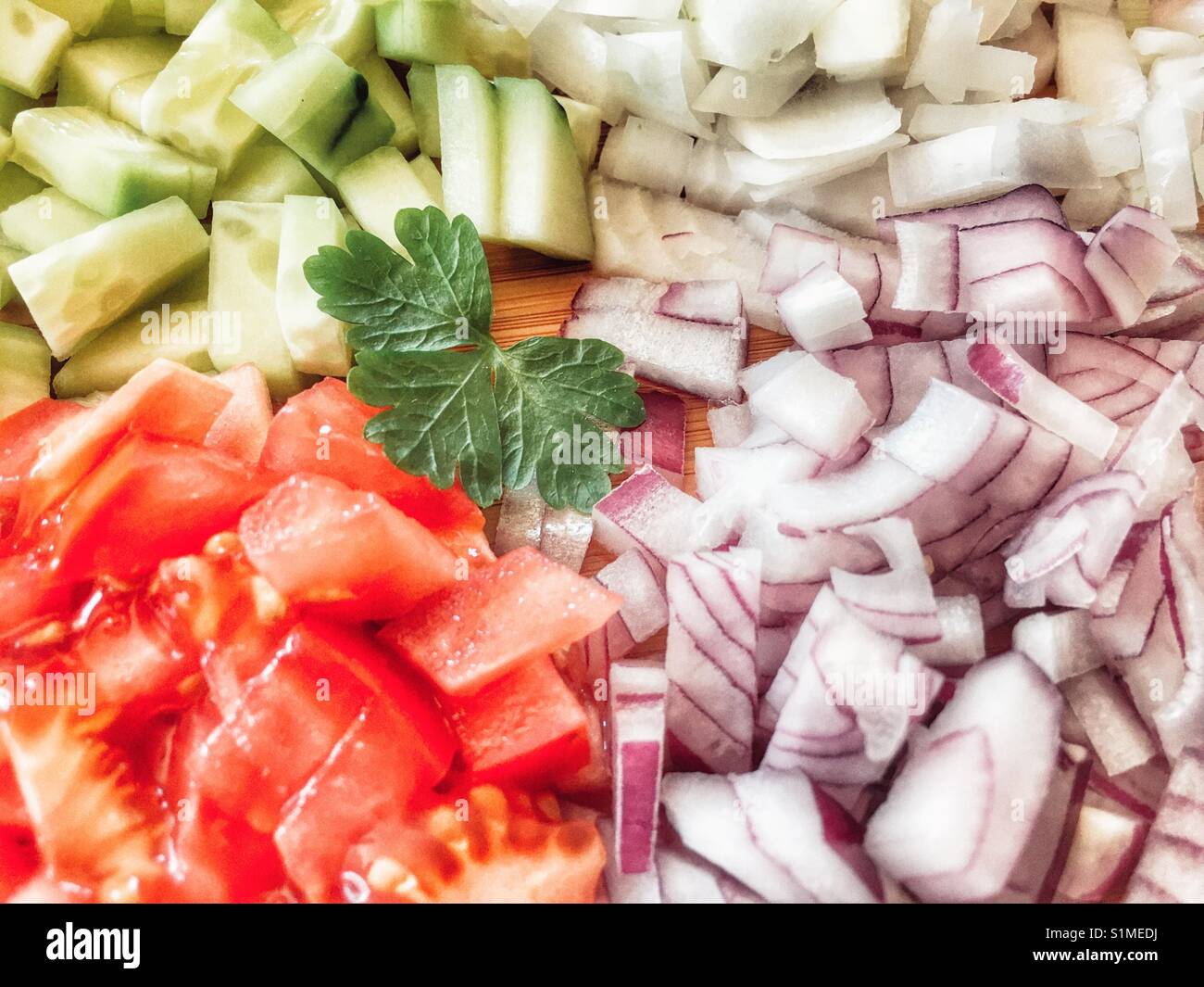 Zutaten auf ein Schneidebrett. Rote Zwiebel, weiße Zwiebel, Gurke, Tomaten und Petersilie - Smartphone-aufgenommenes Stockfoto
