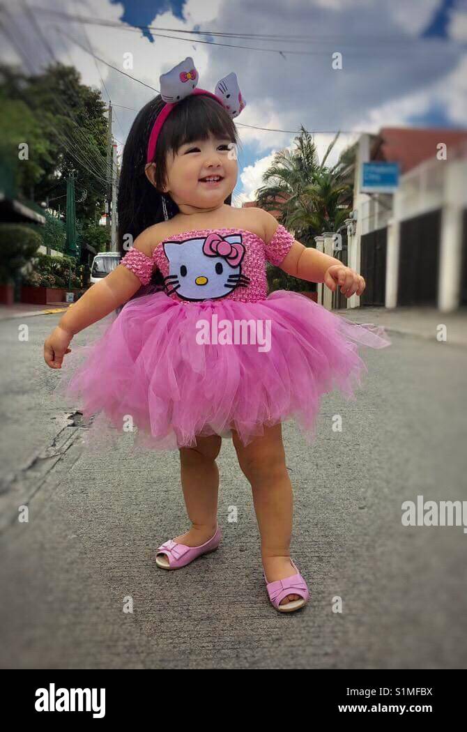Kichernd Baby mit ihren niedlichen rosa hello kitty Tutu Kleid und Puppe Schuhe Stockfoto